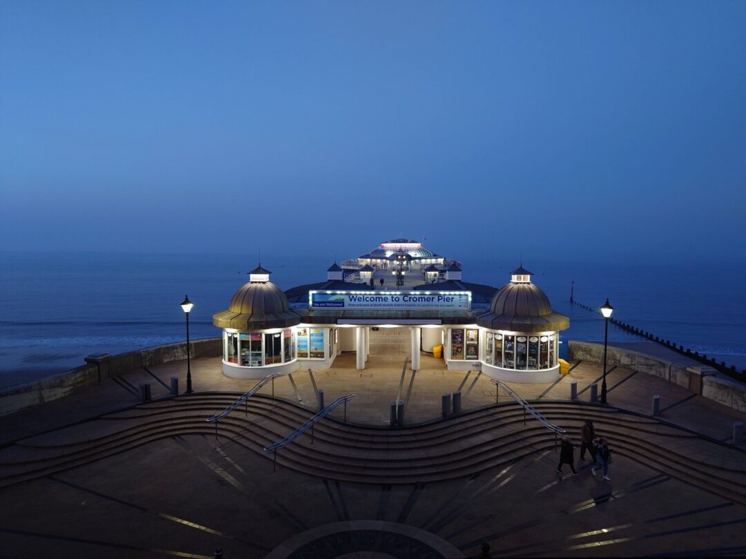 Cromer Pier at dusk. A moody photo showing the entrance amidst a wash of moody blue sea and sky.