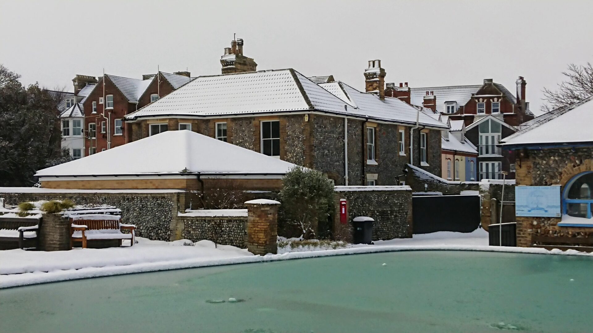 North Cottage Cromer shown dusted withca light covering of snow. The frozen boating pond of North Lodge Park, Cromer, is in the foreground.